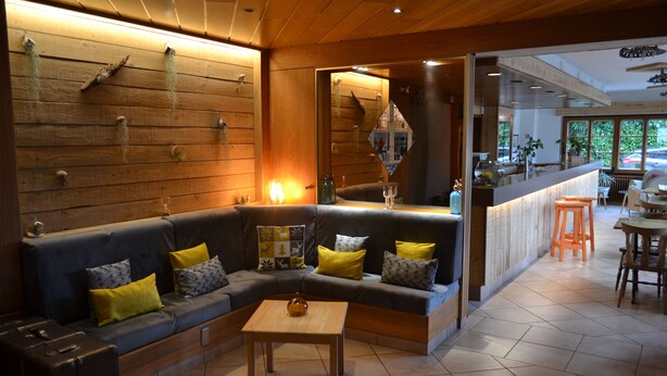 Un intérieur moderne avec un plafond en bois, un canapé d’angle agrémenté de coussins, une petite table en bois et un coin bar avec des tabourets.