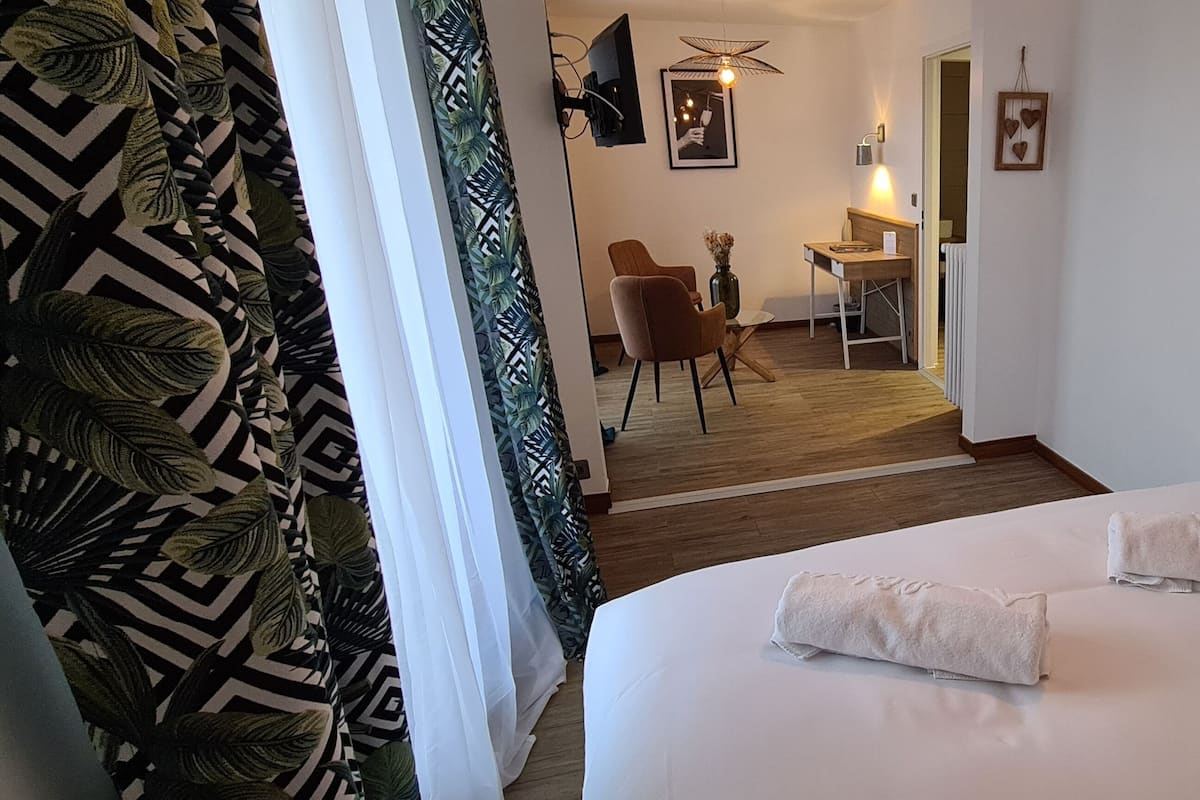 Une chambre d’hôtel avec un lit, deux serviettes, une chaise, une petite table, un tableau au mur et une plante.