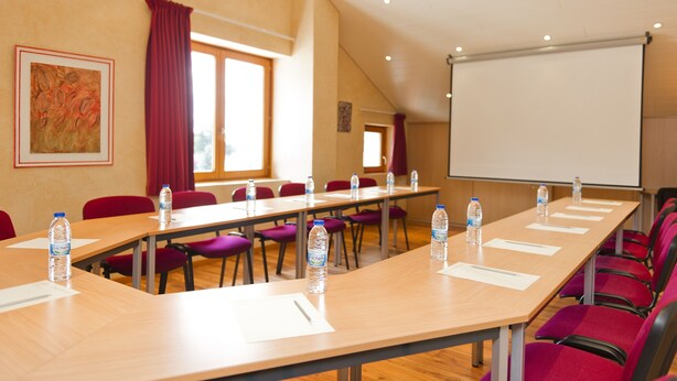 Une salle de conférence avec de longues tables, des chaises rouges et des bouteilles d’eau.