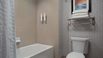 A bathroom with a bathtub, toilet, and a shower area. There are toiletries on the wall and a towel rack above the toilet.