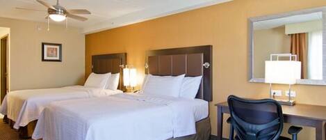 A hotel room with two beds, a desk, a chair, a ceiling fan, and a lamp.