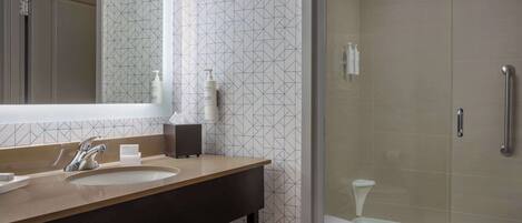A modern bathroom with a large mirror, two sinks, and a glass-enclosed shower.
