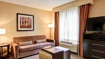 A hotel room with a sofa, a TV, a lamp, and a large window with curtains.