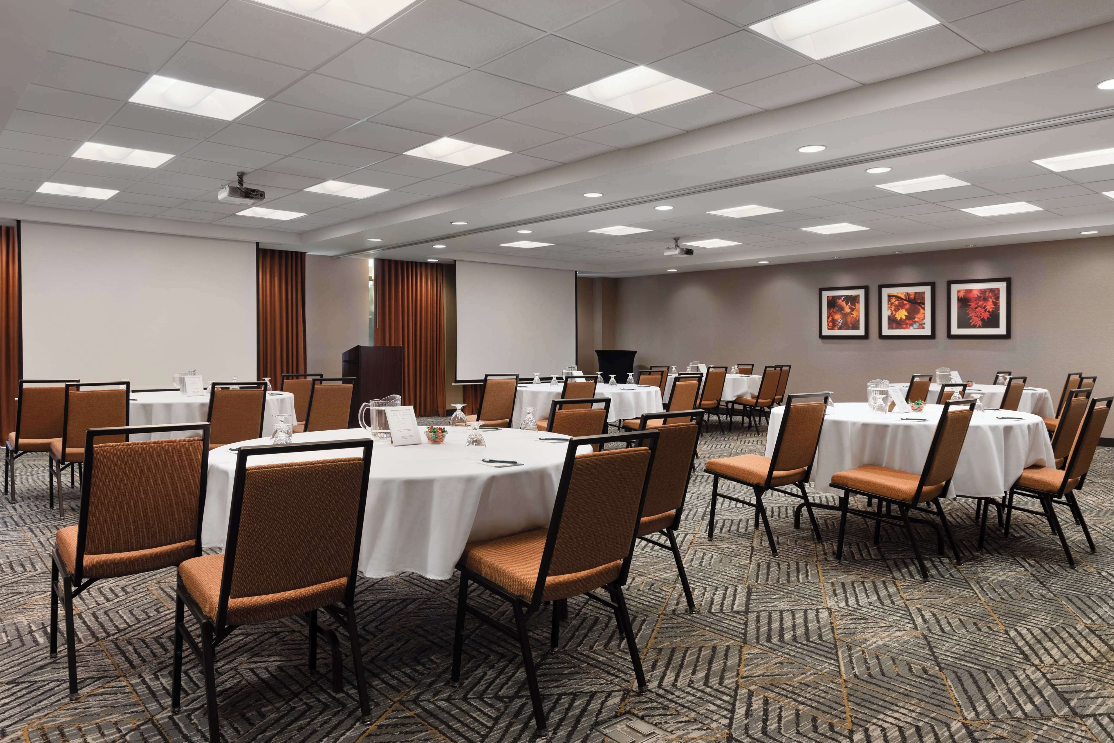 A conference room with multiple round tables, chairs, and a projector screen.