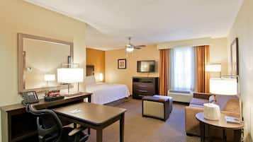 A hotel room with a bed, desk, chair, television, and a small seating area.