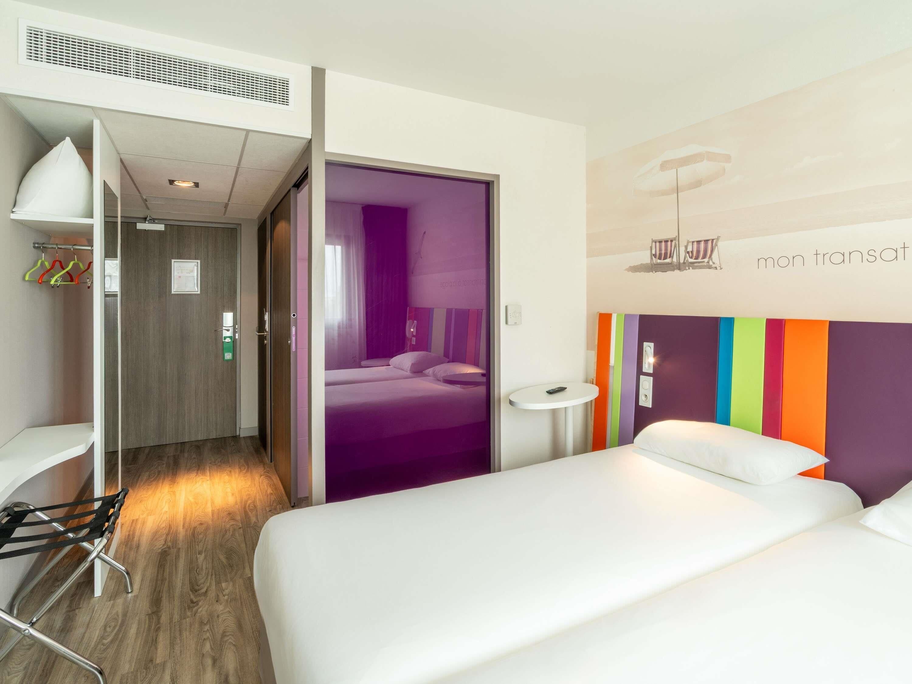 A hotel room with a bed, a bedside table, a chair, a wardrobe, and a bathroom.