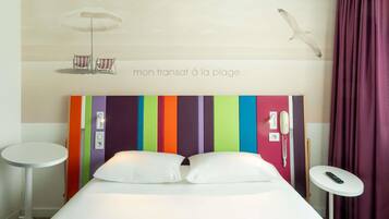 A hotel room with a bed, a small round table, a telephone, and a wall with a striped pattern and a seagull illustration.