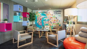 Un hall d’hôtel moderne avec une fresque murale colorée représentant une carte, des coins salon et un lampadaire.