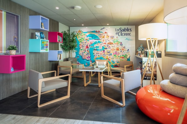 Un vestíbulo de hotel moderno con un mural de mapa colorido, zonas de estar y una lámpara.