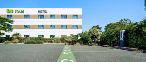 A hotel building with a clear sky, a parking lot with a handicapped parking space, and a sign for 'ibis styles' hotel.
