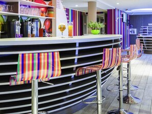 A bar area with striped barstools, a counter with various drink dispensers, and a potted plant.