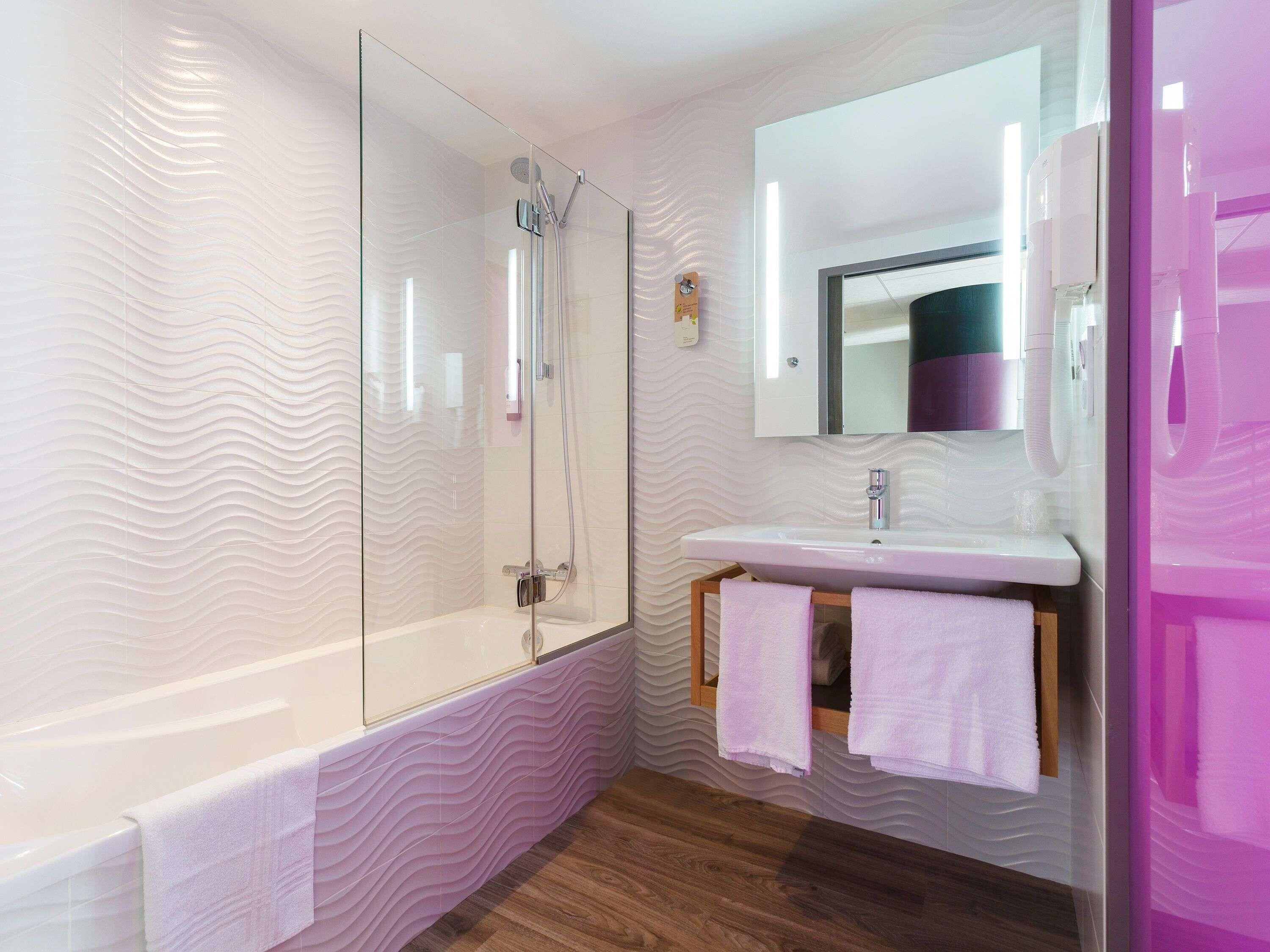 Un baño moderno con ducha envuelta en vidrio, un lavamanos blanco y un mueble de tocador de madera.