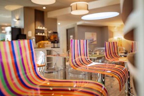 Een moderne eetruimte met kleurrijke gestreepte stoelen en een bar op de achtergrond.
