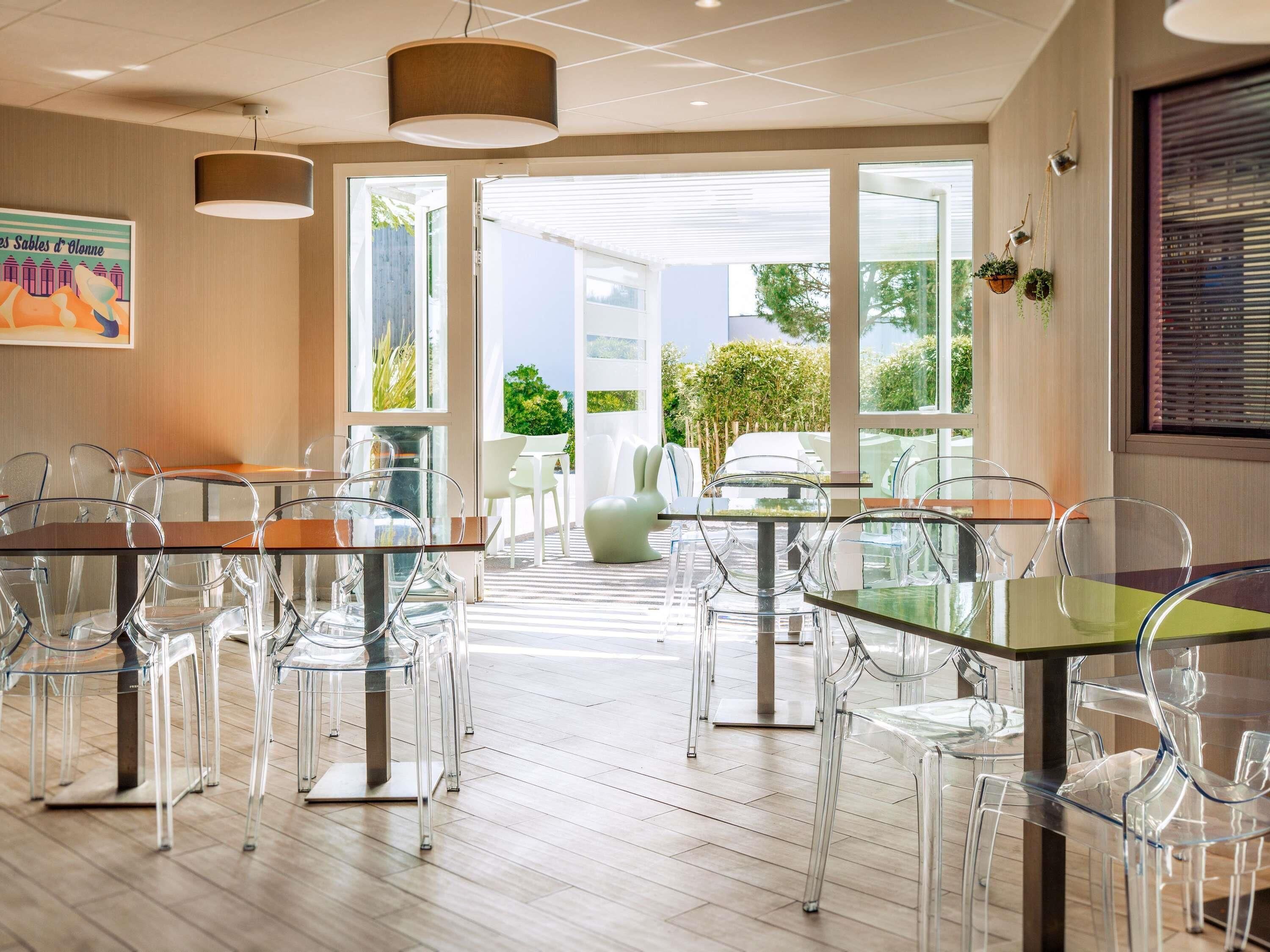 Una moderna camera d'albergo con zona pranzo, tavoli e sedie in vetro, ampie finestre e vista sull'esterno.