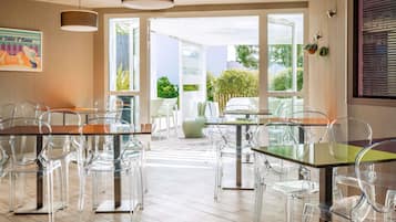 Una moderna camera d'albergo con zona pranzo, tavoli e sedie in vetro, ampie finestre e vista sull'esterno.