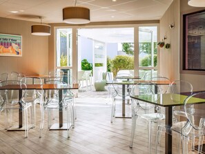 Une chambre d’hôtel moderne dotée d’un coin repas avec des tables et des chaises en verre, de grandes fenêtres et une vue sur l’extérieur.