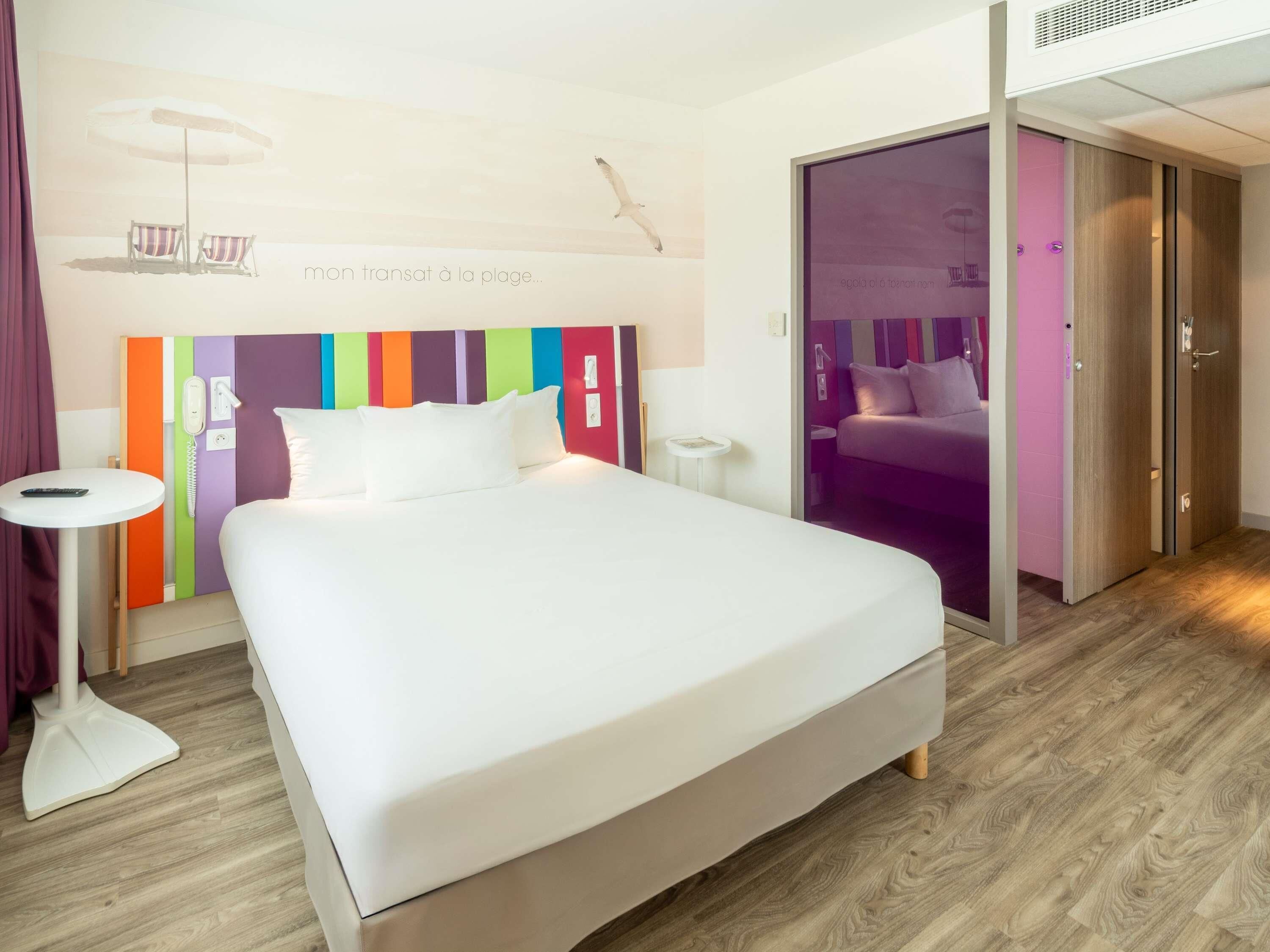 A modern hotel room with a large bed, a bedside table, a phone, and a view of a beach.