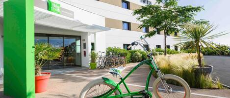 A hotel named 'ibis styles' with a modern design, a bicycle parked in front, and potted plants around.