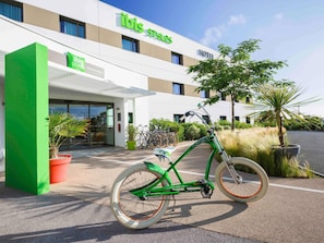 Un hôtel appelé « ibis Styles », doté d’un design moderne, avec un vélo garé devant et des plantes en pot disposées tout autour.