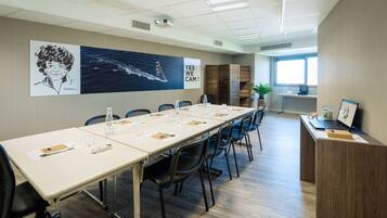 Uma sala de conferências com uma mesa comprida, cadeiras e uma escrivaninha com um laptop e uma moldura com uma fotografia.