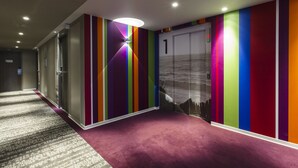 Un couloir avec une moquette violette, un mur à rayures verticales et une porte portant le numéro 1.