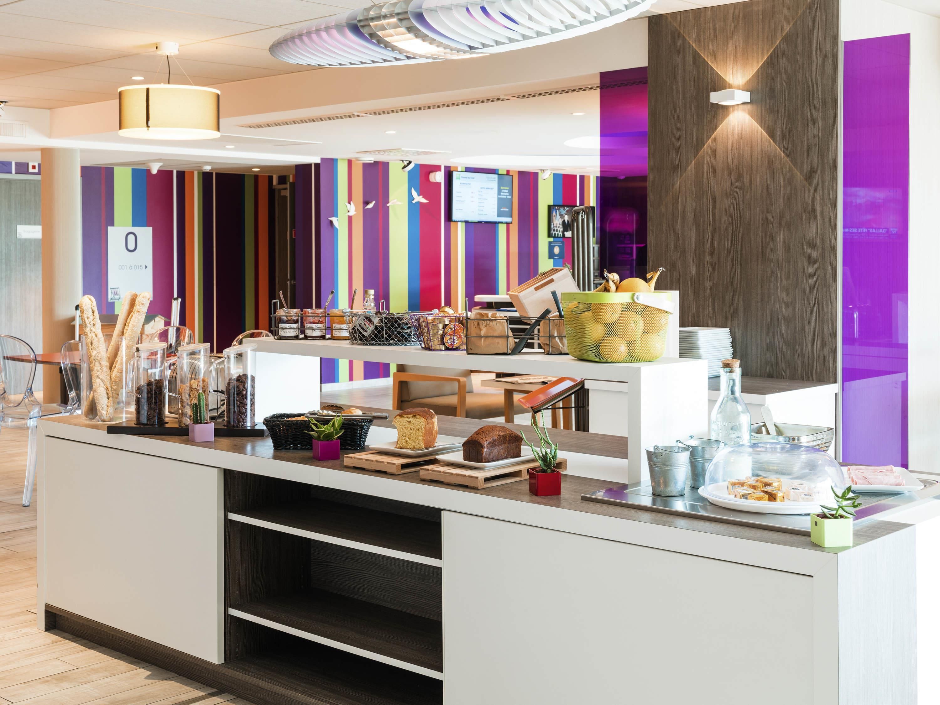 Una barra de desayuno moderna con diversos alimentos y una pared de rayas coloridas al fondo.