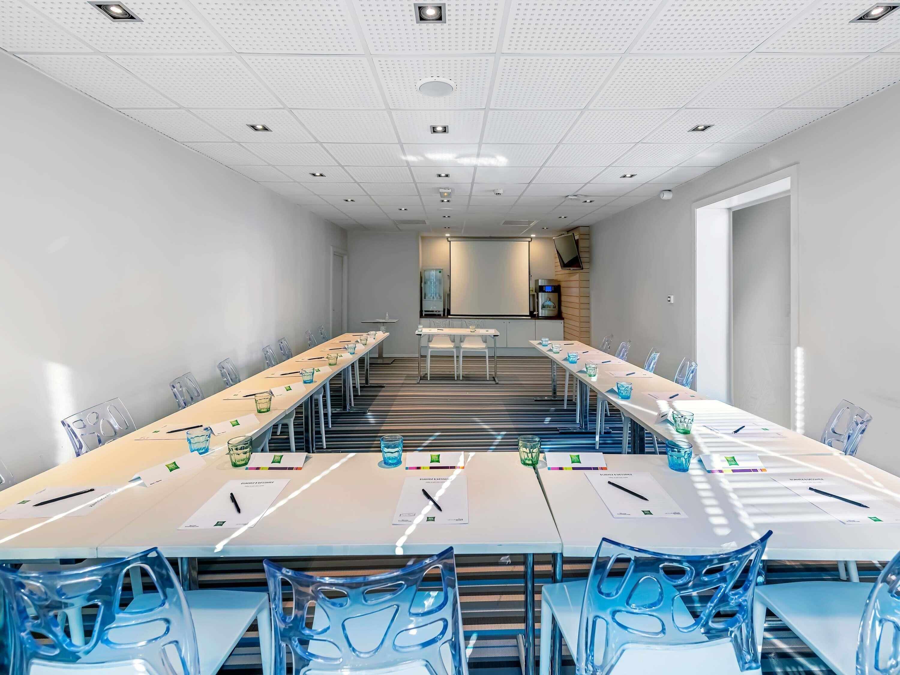 Ein Konferenzraum mit einem langen Tisch, Stühlen und einer Projektionsleinwand.