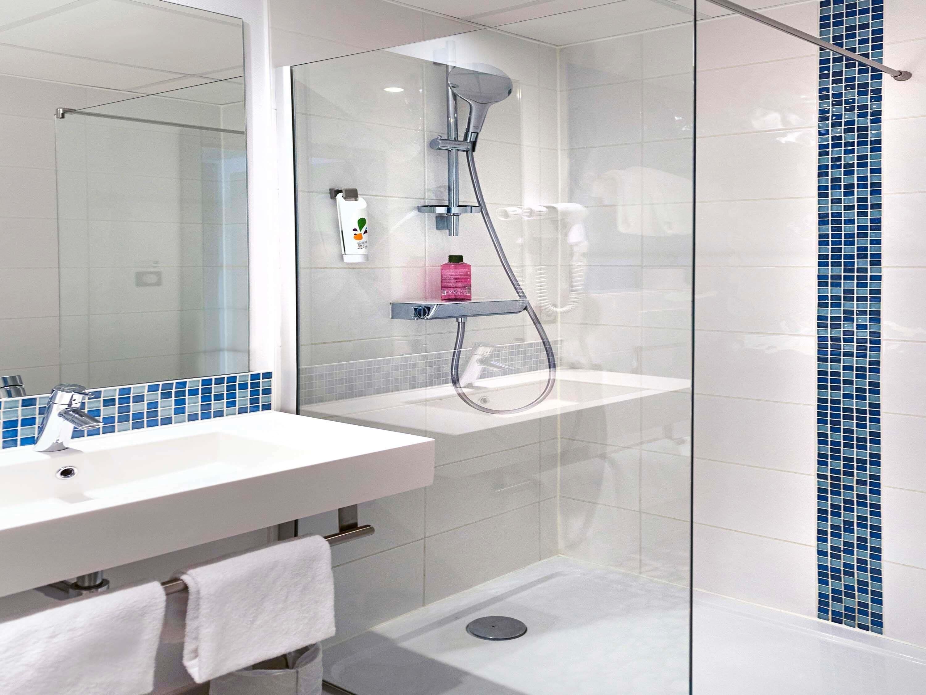 A modern bathroom with a glass shower enclosure, a white sink with a mirror, and a tiled backsplash.