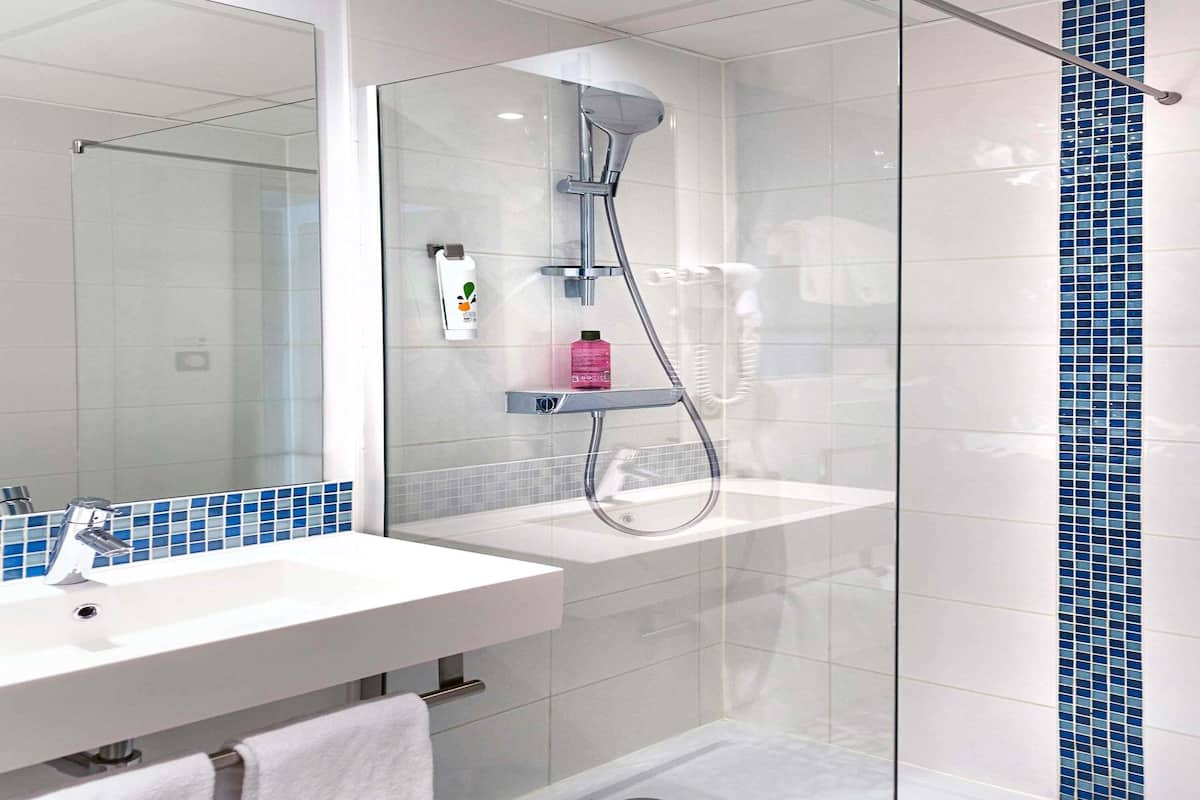 Un baño moderno con cabina de ducha de vidrio, un lavamanos blanco con espejo y un salpicadero de azulejos.