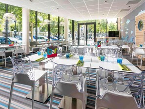 A modern restaurant with clear glass chairs and tables, large windows, and a view of the street outside. - ibis Styles Strasbourg Avenue du Rhin (Strasbourg)