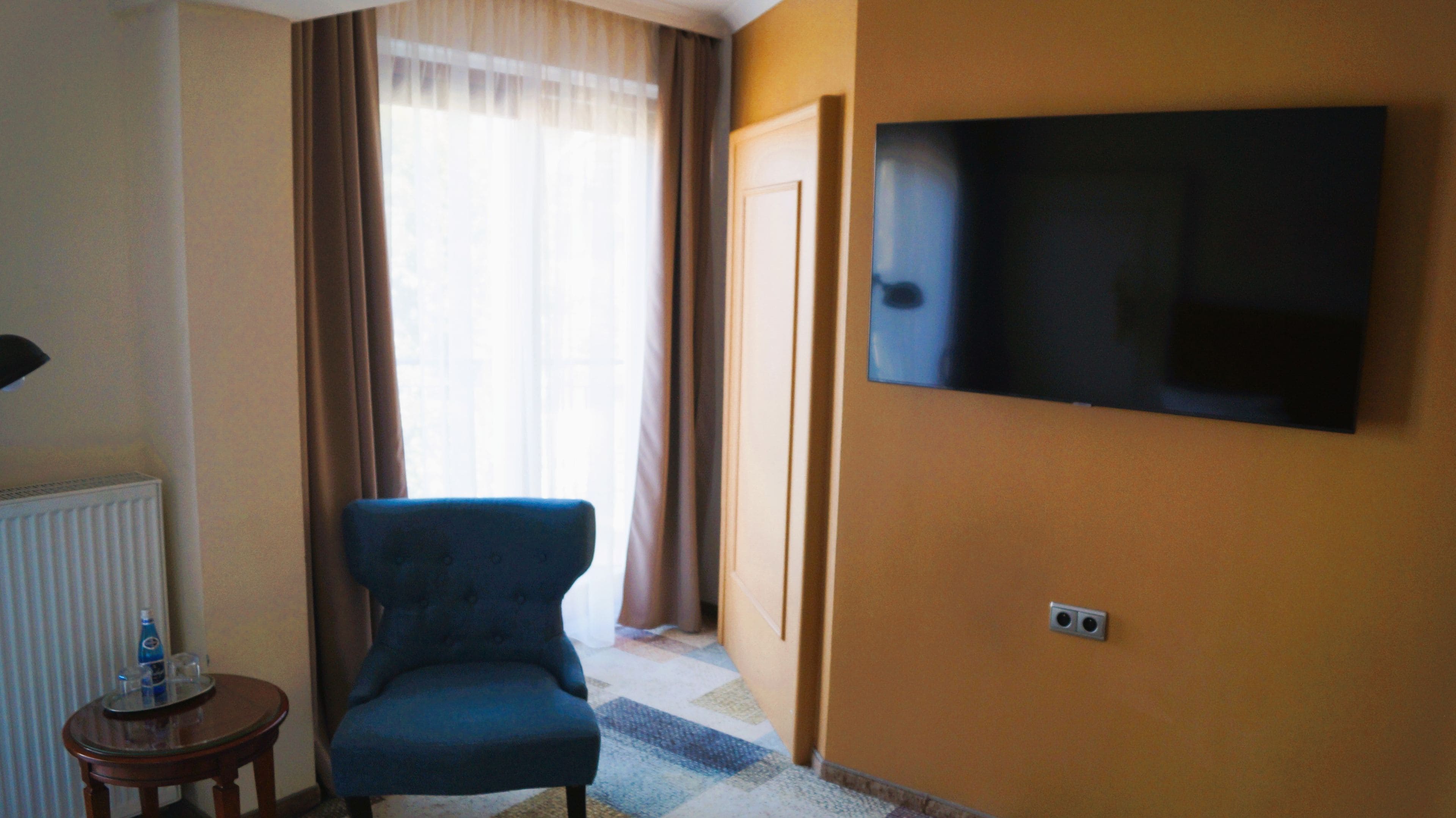 Une pièce avec un fauteuil bleu, un téléviseur fixé au mur et un radiateur.