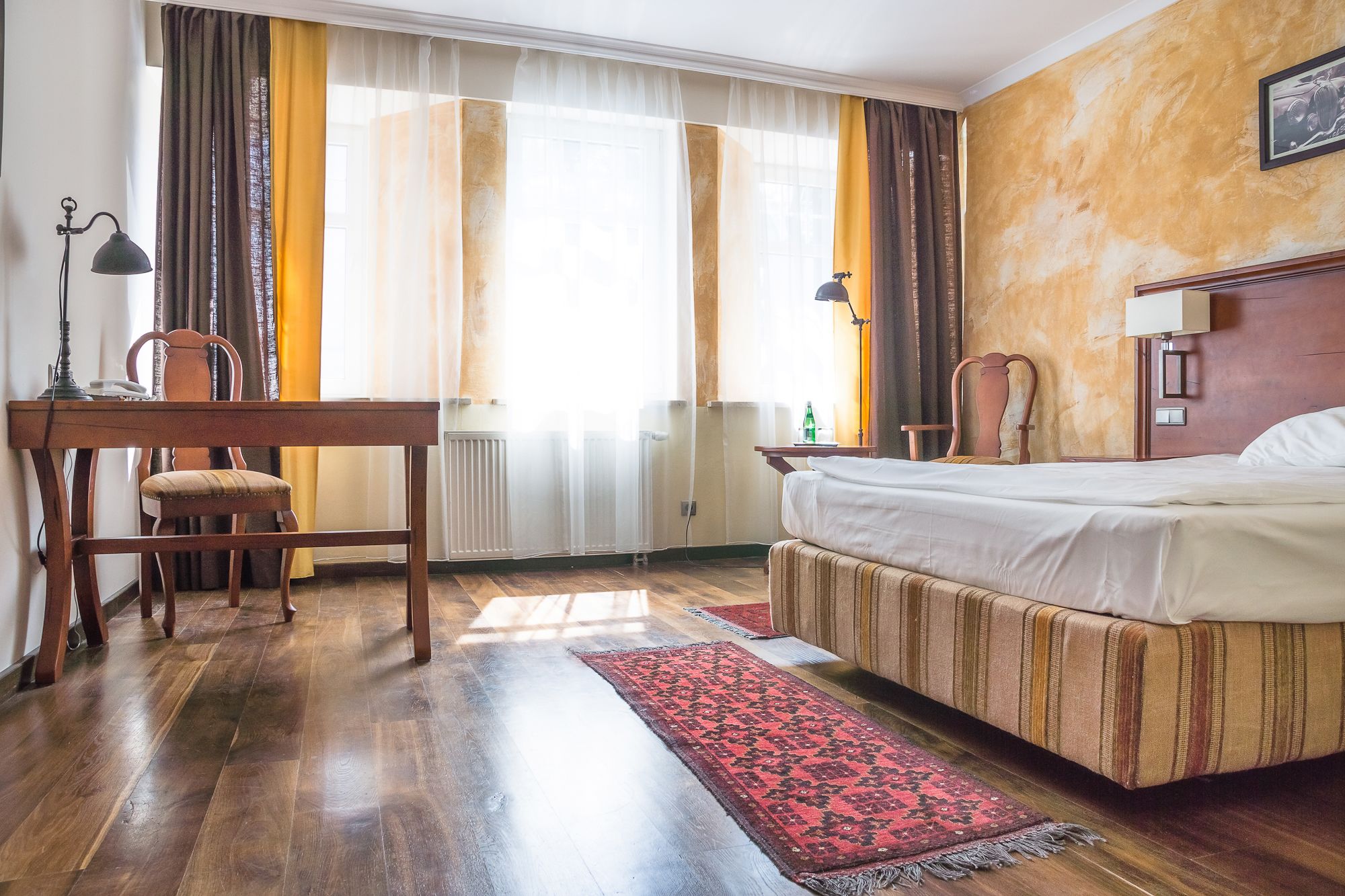 A hotel room with a bed, a desk, a chair, and a window with curtains.