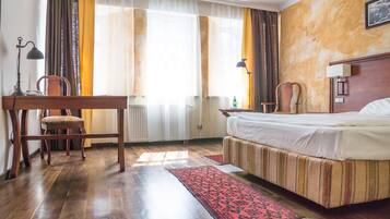 A hotel room with a bed, a desk, a chair, and a window with curtains.