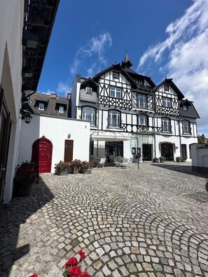 A traditional half-timbered building with a cobblestone courtyard, a red door, and a covered outdoor seating area.