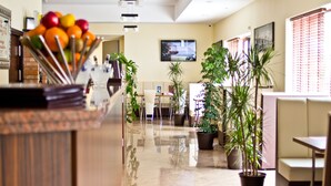Un hall d’hôtel comprenant un comptoir d’accueil, des plantes en pot, des espaces aménagés avec des sièges et un écran de télévision.