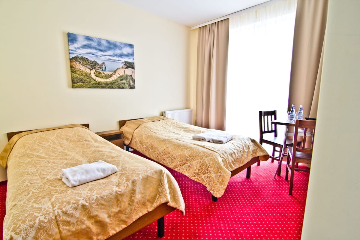 Habitación de hotel con dos camas, una mesa de comedor, sillas, un cuadro en la pared y una ventana con cortinas.