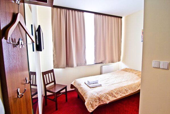 A hotel room with a bed, a chair, a desk, and a window with curtains.