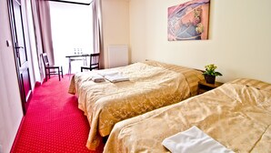 Une chambre d’hôtel avec deux lits, une moquette rouge, un bureau avec une chaise, un radiateur et un tableau au mur.