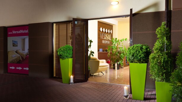 Un espace d’accueil d’hôtel au design moderne, comprenant un comptoir d’accueil, un coin salon et des plantes en pot.