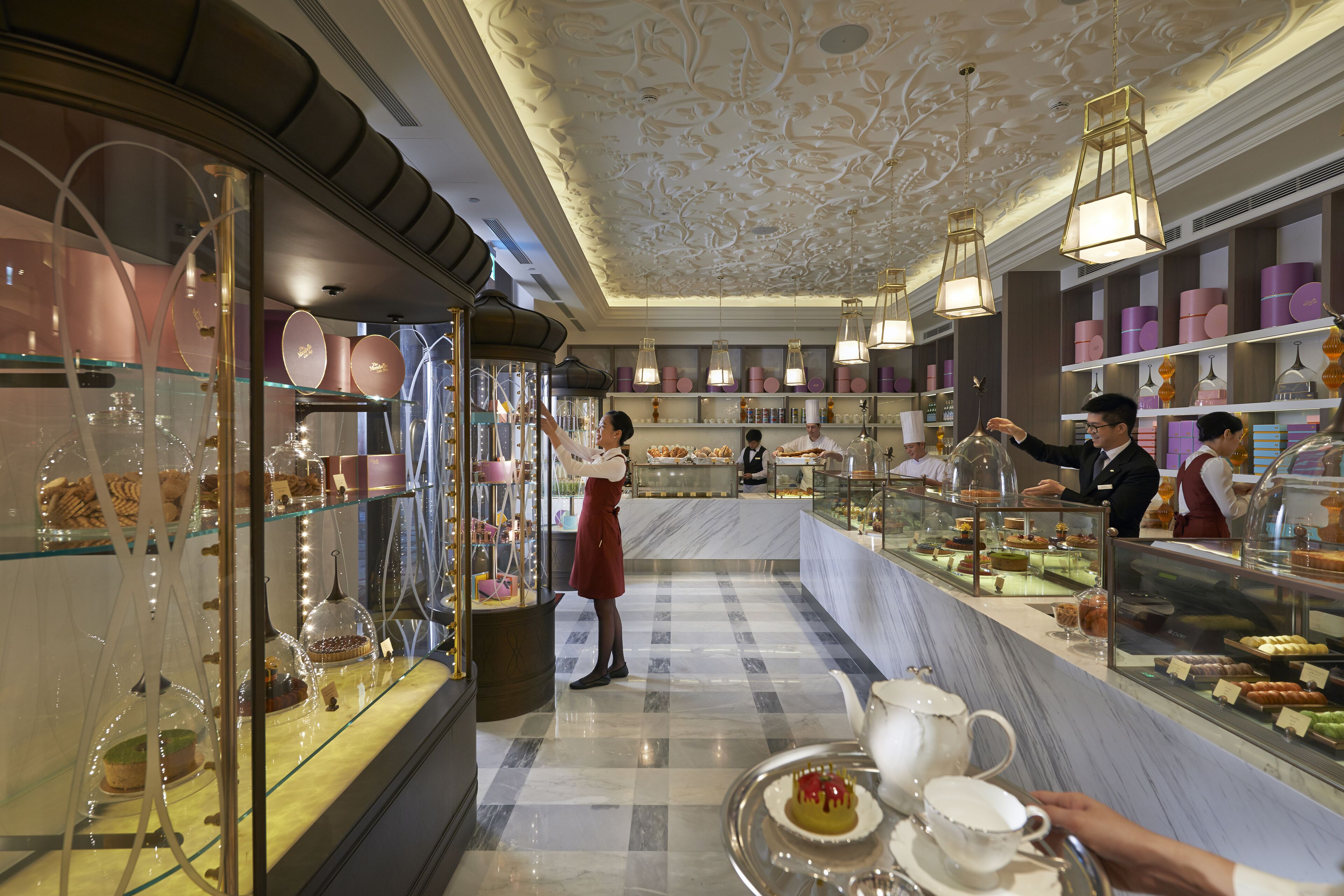 A bakery counter with pastries and desserts, a person serving, and a tea service setup.