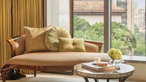 A modern living room with a sofa, a round coffee table, and a large window offering a view of a building with a tiled roof. - Mandarin Oriental, Taipei (Taipei)