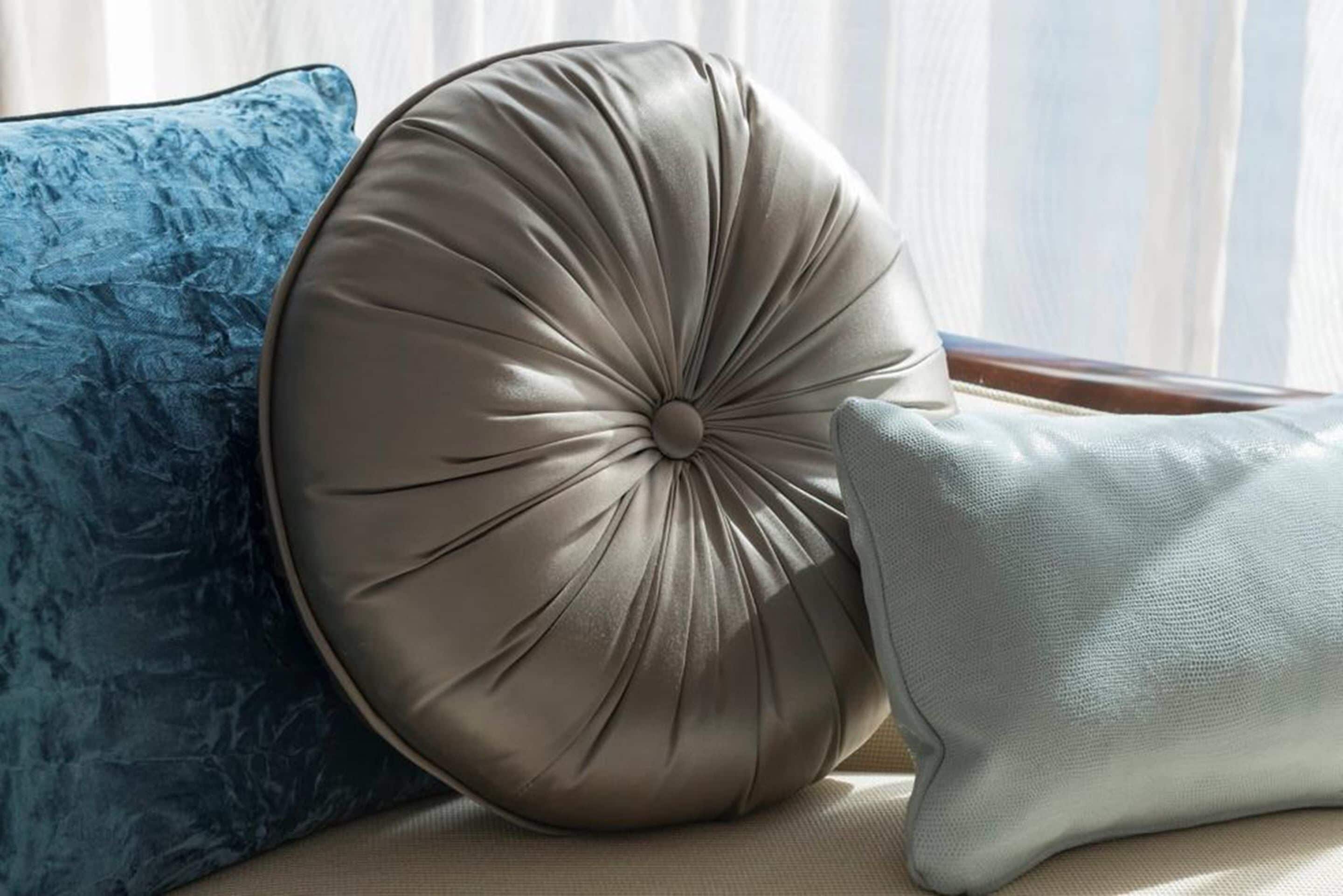 A beige upholstered headboard with a tufted design, a blue textured pillow, and a plain light-colored pillow.