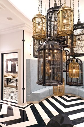Interior moderno com piso estampado em preto e branco, um sofá cinza e várias luminárias pendentes em estilo gaiola de pássaro.