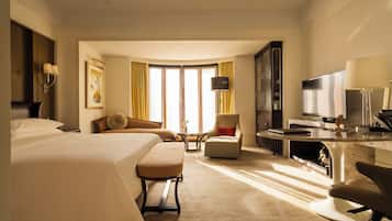 Habitació d'hotel amb llit, escriptori, cadira, sofà, televisió i finestra amb cortines.