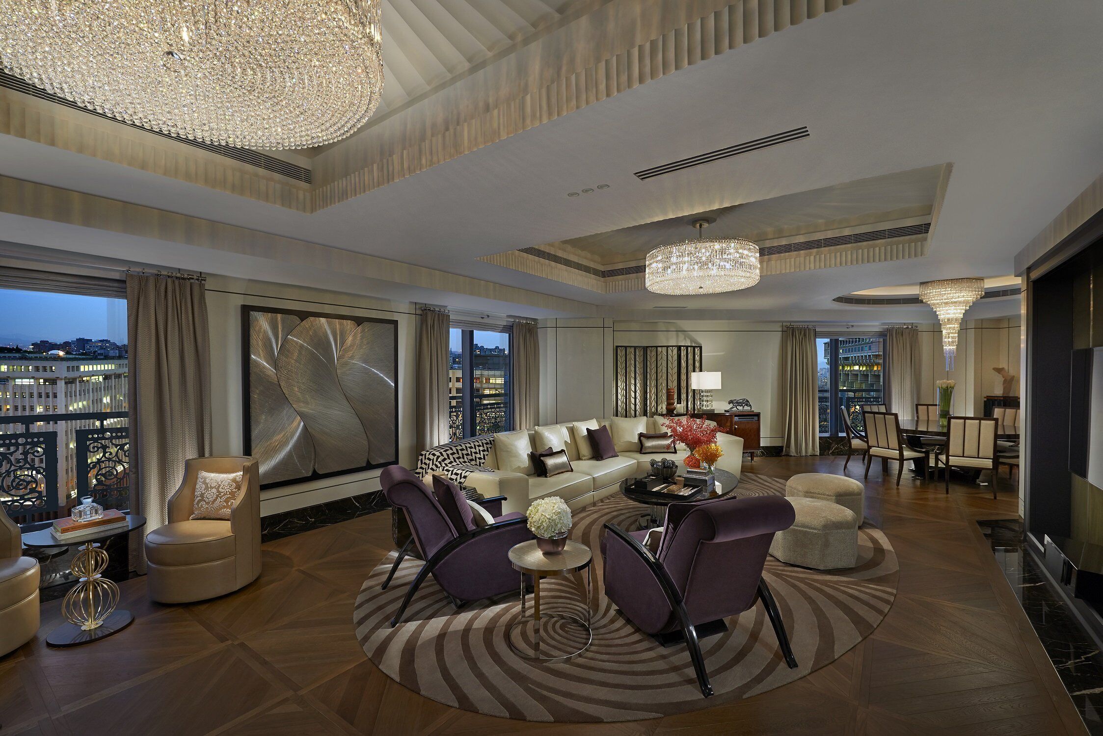 A spacious living room with a large window, a chandelier, and a view of the cityscape.