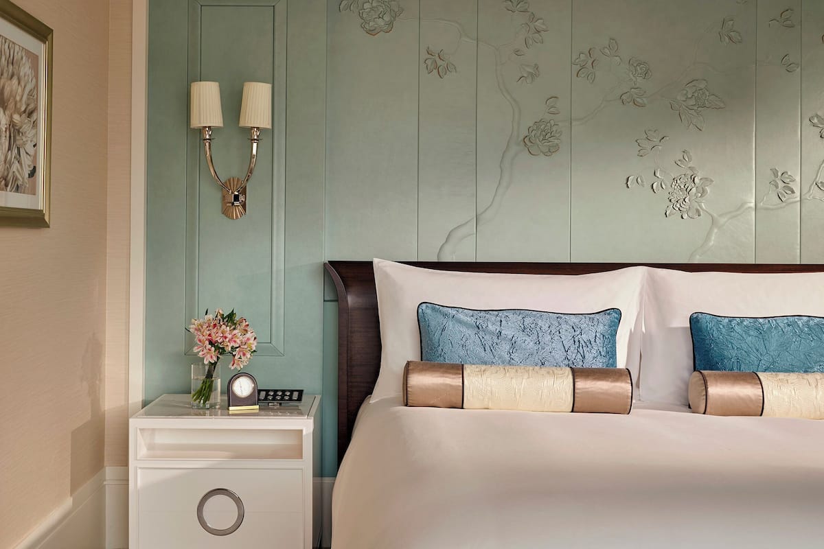 Ein Schlafzimmer mit Bett, Nachttisch, Wandlampen und einem floralen Wanddesign.