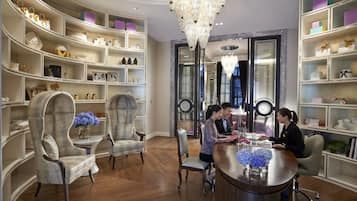 A luxurious room with a curved bookshelf, elegant chairs, a round wooden table, and a chandelier.