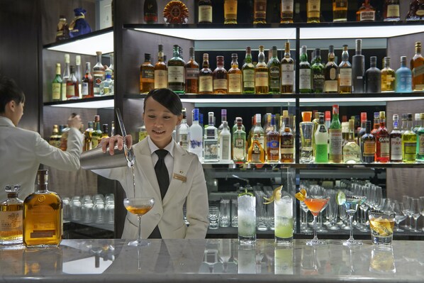 A bar with a bartender preparing drinks, shelves of liquor bottles, and various glasses on the counter. - Mandarin Oriental, Taipei (Taipei)