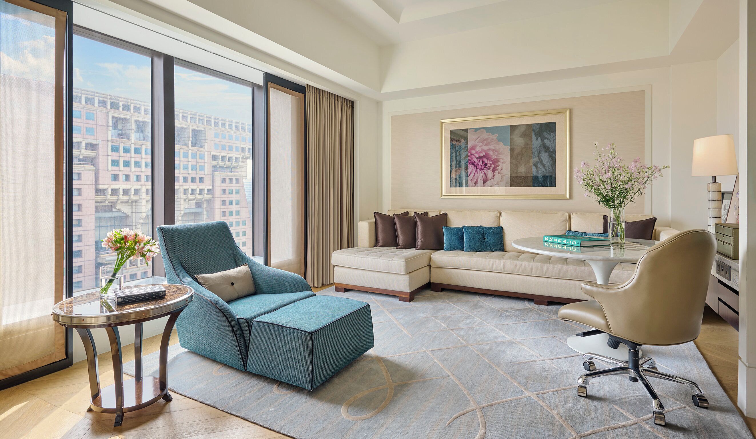 A modern hotel room with a large window, a sofa, a chair, a small table, and a lamp.