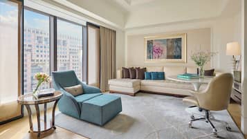 A modern hotel room with a large window, a sofa, a chair, a small table, and a lamp.